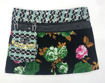 May include: A black mini skirt with a floral print featuring green, white, and pink roses. The skirt has a unique design with a zippered pocket and a decorative waistband with silver studs and a geometric pattern.
