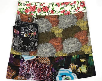May include: A multi-layered skirt with a floral print. The top layer is a white background with pink flowers. The middle layer is a brown background with a floral pattern. The bottom layer is a black background with a colorful floral pattern. The skirt has a small black pocket with a zipper on the left side.