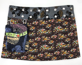 May include: A brown mini skirt with a floral print and a black pocket with a feather design. The skirt has a gray waistband with silver studs.