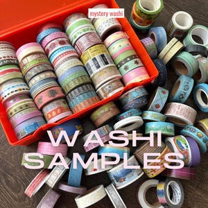 May include: An assortment of washi tape samples in an orange container and scattered on a wooden surface. The tapes feature various colors and patterns, including floral, geometric, and text designs. The text "WASHI SAMPLES" is displayed in pink.