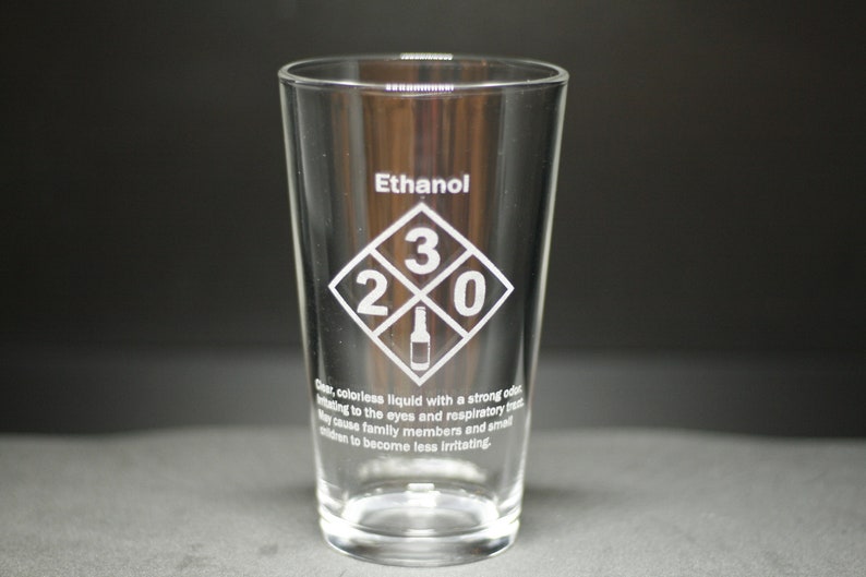 May include: A clear glass pint glass with the word "Ethanol" and a diamond-shaped symbol with the numbers "2 3 0" and a bottle icon inside. The text below the symbol reads: "Clear, colorless liquid with a strong odor irritating to the eyes and respiratory tract. May cause family members and small children to become less irritating."