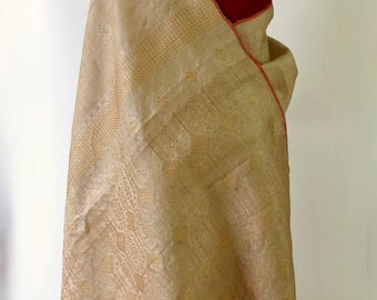Può includere: Un sari di seta beige con un motivo ricamato in oro e argento. Il sari ha un bordo rosso e una frangia sul fondo.