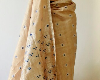 Può includere: Un sari beige con motivi floreali blu e un bordo argentato è drappeggiato su un manichino. Il sari è abbinato a un top all'americana in pizzo nero. Il tessuto ha una lucentezza sottile e il design è tradizionale.