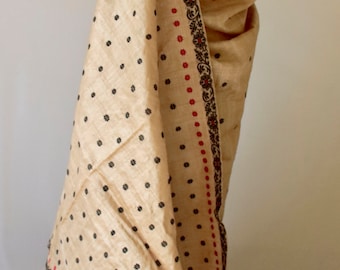 Può includere: Un sari beige con un motivo floreale nero e un bordo decorativo con disegni floreali rossi e neri. Il sari è drappeggiato su un manichino, rivelando un top in pizzo nero.
