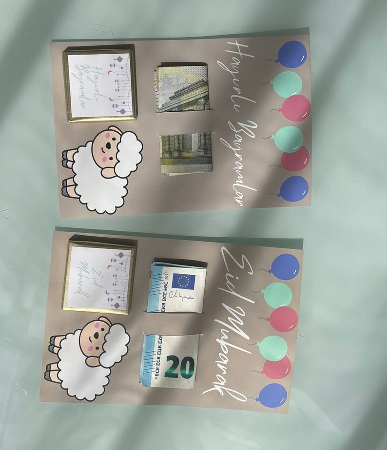 May include: Two cards with a light brown background, each with a white sheep illustration, a small gold frame with text, and a stack of euro bills. The top card has the text "Happy Holidays" in white lettering and five balloons in blue, pink, and green. The bottom card has the text "Eid Mubarak" in white lettering and four balloons in blue, pink, and green.
