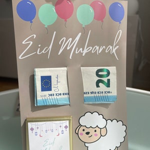 May include: A light brown card with the text "Eid Mubarak" in white cursive writing. There are five colorful balloons at the top of the card. The card has two 20 euro bills, a chocolate bar with the text "Eid Mubarak" and a cartoon white sheep.