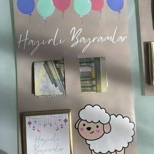 May include: A light brown card with the text "Hayirli Bayramlar" in white. The card is decorated with blue, pink, and green balloons. There are two folded bills of money on the card. There is a small gold frame with the text "Hayirli Bayramlar" in purple and a white cartoon sheep.