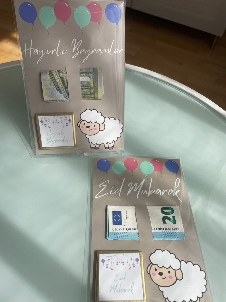 May include: Two cards with a light brown background and a white sheep illustration. The top card has the text "Hayırlı Bayramlar" and the bottom card has the text "Eid Mubarak". Both cards have colorful balloons and a small square with the text "Hayırlı Bayramlar" and "Eid Mubarak" respectively.