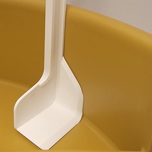 May include: A white plastic scoop with a handle, sitting inside a yellow plastic container.