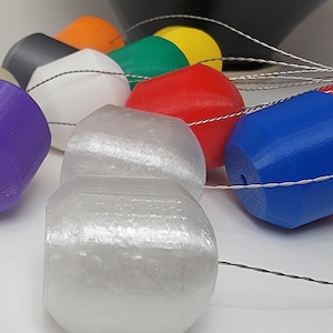 Op de afbeelding: Een verzameling kleurrijke, cilindervormige objecten met een gat aan één uiteinde, verbonden door dunne, zilveren draden. De objecten zijn in verschillende kleuren, waaronder paars, wit, rood en blauw. De objecten lijken van plastic te zijn.