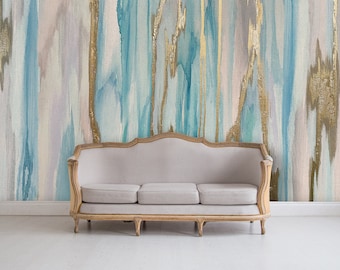 May include: A light-colored, three-cushion sofa with a wooden frame sits in front of a wall with an abstract painting. The painting features vertical brushstrokes in shades of blue, gold, and white.
