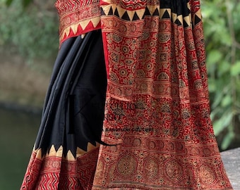 May include: A black and red saree featuring intricate block-printed patterns in wavy lines and geometric shapes. The garment includes a solid black section, a wide border with a triangular motif, and a metallic gold hem at the bottom edge.