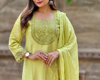 May include: A light green, embroidered salwar kameez set. The long-sleeved top features intricate embroidery around the neckline and cuffs. A matching dupatta is draped over the shoulder. The outfit is a solid color with a subtle sheen.