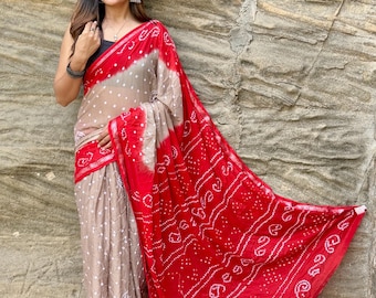 May include: A traditional Indian saree with a beige and red color scheme. The saree features a dotted pattern on the beige fabric and a detailed design on the red fabric. The saree is draped over a person.