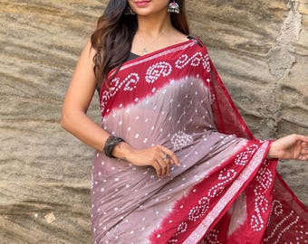 May include: A woman wearing a traditional Indian saree. The saree features a maroon and mauve color scheme with white dot patterns. The border is a darker maroon with white geometric designs. The woman is wearing silver earrings and a black top.