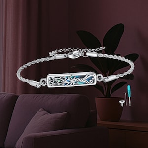 Può includere: Bracciale in argento con un ciondolo rettangolare con un design ad albero della vita con accenti blu e verdi. Il bracciale ha una catena a corda e una chiusura a fermaglio. Include un piccolo set di attrezzi.