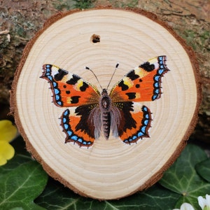 May include: A painted wooden slice featuring a detailed image of a butterfly with orange, black and blue wings.