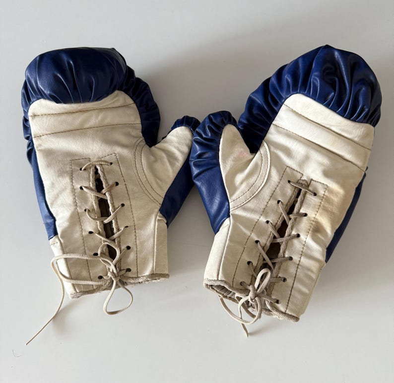 May include: A pair of white boxing gloves with blue trim and lace-up closures. The gloves are worn and show signs of use.