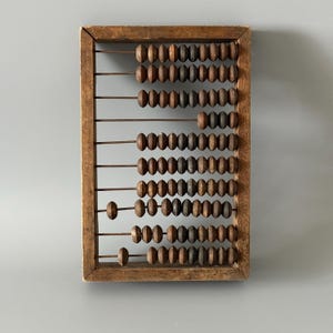 May include: A vintage wooden abacus with a rectangular frame and rows of wooden beads. The beads are various shades of brown and gray, and the frame has a weathered appearance. The abacus is a classic educational tool.