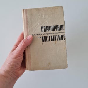 Puede incluir: Un libro vintage de color beige con el título "Справочник по математике" (en ruso: "Manual de matemáticas") impreso en negro en la portada. El libro está escrito por A.P. Rybkin, A.Z. Rybkin y A.G. S. Khrenov.
