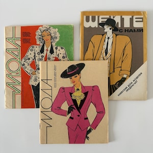 May include: Three vintage fashion magazines with illustrations of stylish outfits. The magazines feature bold graphics and text, with a color palette including red, green, yellow, and pink. The covers showcase illustrations of women in fashionable attire.