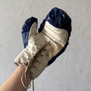 May include: A white and blue boxing glove with a lace-up closure. The glove is made of leather and has a traditional design.