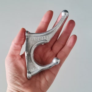 May include: Silver metal hook with the text "APPM3" on the side. The hook is designed for hanging items.