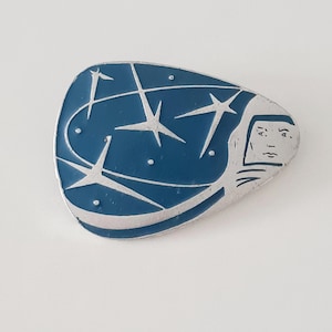 Könnte beinhalten: Eine silberne und blaue Emaille-Anstecknadel in Form eines Raumschiffs mit Sternen und dem Text "AI AS" an der Seite.