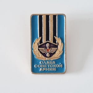 May include: A rectangular pin with a blue background and gold trim. The pin features a central emblem with a red star, wings, and a laurel wreath. The text "Glory to the Soviet Army" is written in Cyrillic.