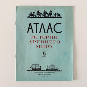 Puede incluir: Una portada de libro de texto vintage en azul claro con el título "ATLAS" en letras negras grandes. Debajo, en rojo, "HISTORIA DEL MUNDO ANTIGUO". El número "5" es prominente. Se incluyen ilustraciones de guerreros y barcos.