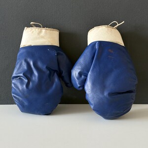May include: A pair of blue boxing gloves with white cuffs. The gloves are made of a faux leather material.
