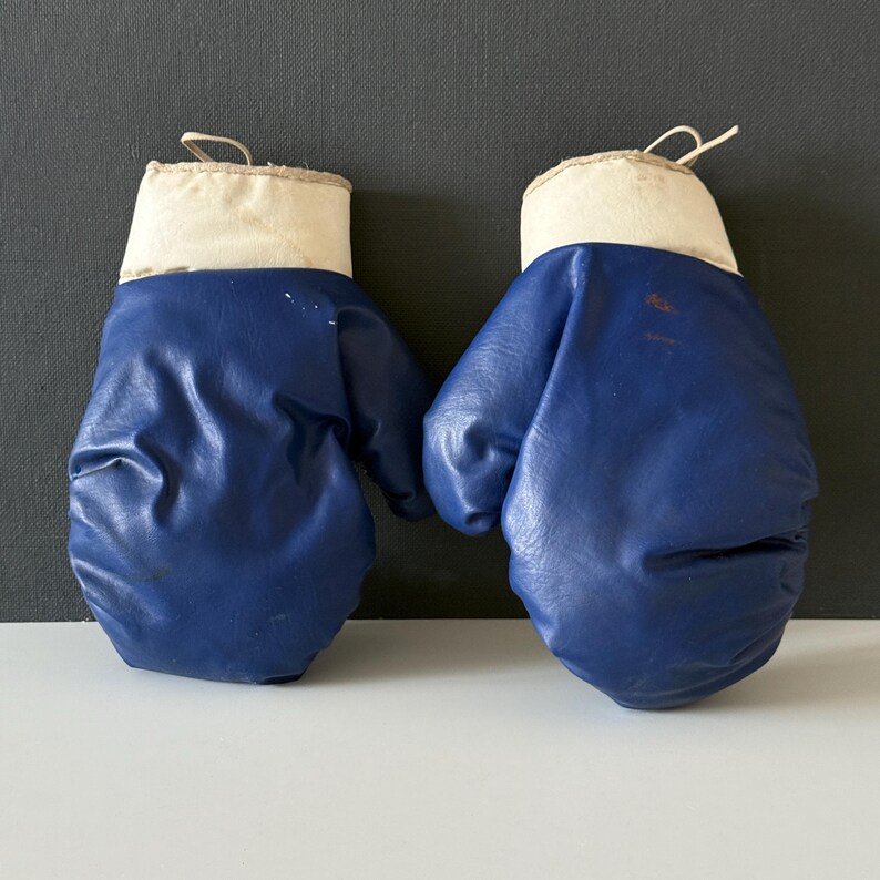 May include: A pair of blue boxing gloves with white cuffs. The gloves are made of a faux leather material.
