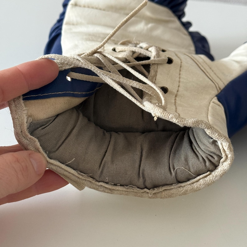 May include: Close-up of the inside of a white and blue boxing glove. The glove is laced up and has a padded interior.
