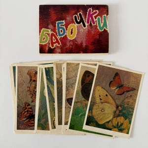 Puede incluir: Un juego de cartas de mariposas vintage con una caja decorativa. La caja tiene la palabra "Mariposas" en letras cirílicas coloridas. Las cartas presentan ilustraciones de varias mariposas en tonos marrones, naranjas y amarillos.