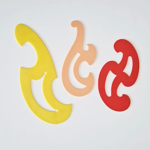 Può includere: Tre righelli a curva francese in plastica gialla, pesca e rossa. Questi strumenti di disegno hanno bordi curvi per disegnare curve fluide. I righelli sono disposti su uno sfondo bianco, mostrando le loro forme distinte.