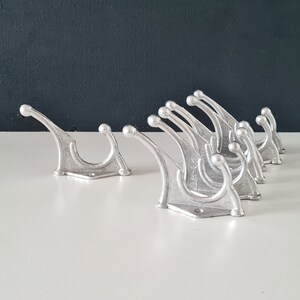 May include: A set of ten silver metal hooks with a unique curved design. The hooks are arranged in a row, with the largest hook at the front and the smallest hook at the back. The hooks are all made of the same metal and have a smooth, polished finish.