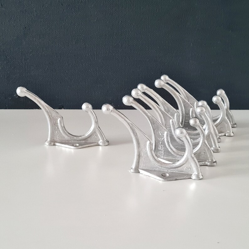 May include: A set of ten silver metal hooks with a unique curved design. The hooks are arranged in a row, with the largest hook at the front and the smallest hook at the back. The hooks are all made of the same metal and have a smooth, polished finish.