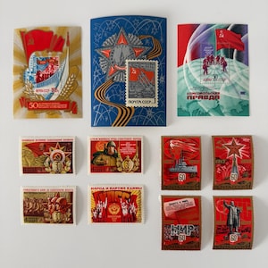Könnte beinhalten: Eine Sammlung von Vintage-Briefmarken und -Umschlägen aus der Sowjetzeit. Die Briefmarken zeigen verschiedene Motive, darunter Flaggen, Militärthemen und Porträts. Farben sind Rot, Gold, Blau und Grün. Einige Briefmarken haben die Zahl "60" und kyrillischen Text.