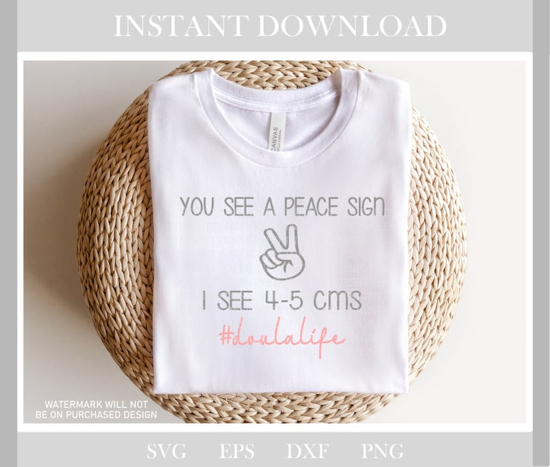 May include: White t-shirt with the text "You see a peace sign, I see 4-5 cms #doulalife" in gray and pink lettering. A peace sign is drawn in gray above the text.