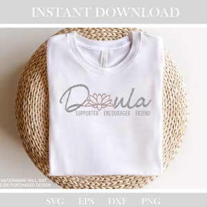 May include: White t-shirt with the word "Doula" in a script font, accompanied by a lotus flower graphic. Below the word are the words "Supporter, Encourager, Friend". The shirt is folded on a woven surface.