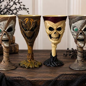 Puede incluir: Cuatro copas decorativas con diseños de personajes distintos: dos copas con temática de momia con ojos verdes y detalles envueltos, una copa marrón inspirada en un espantapájaros con cara cosida y una copa de calavera color crema con cuello rojo oscuro.