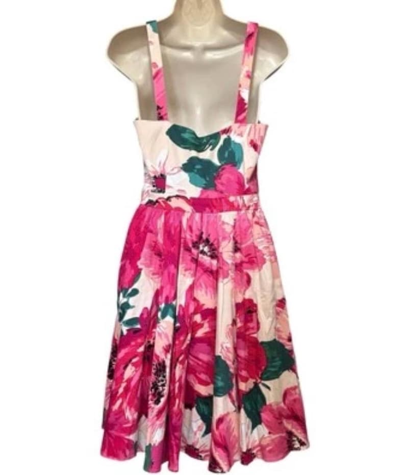 May include: A floral print dress with a fitted bodice and flared skirt. The dress features a pattern of large pink and magenta flowers with green leaves against a cream background. It has a scoop neckline and wide shoulder straps. The dress is sleeveless.
