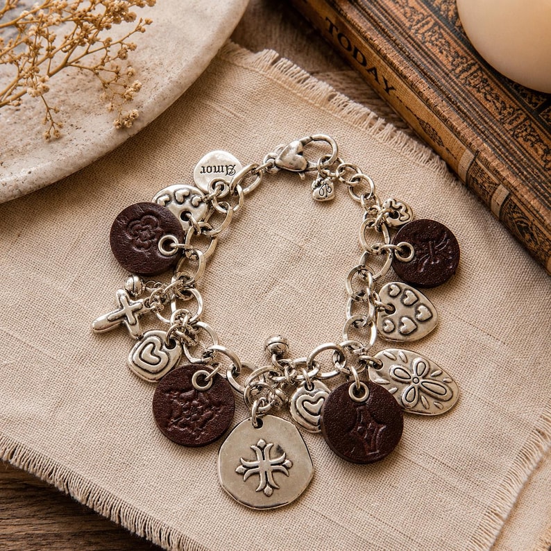 May include: Silver charm bracelet with various charms, including hearts, crosses, and floral designs. The bracelet also features brown leather-like circular charms. The word "Amor" is on one of the charms.