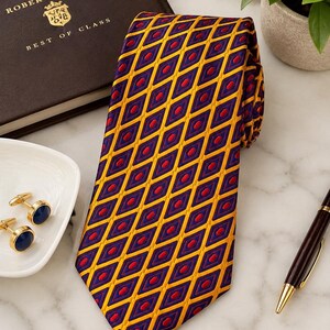 Peut inclure: Une cravate présentant un motif géométrique répétitif en losanges violet foncé et jaune vif, avec de petits accents hexagonaux rouges centrés dans chaque forme de losange. La cravate est fabriquée dans un tissu tissé avec un éclat visible.