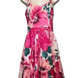 May include: A floral dress with a sweetheart neckline and a full skirt. The dress features a vibrant pattern of large pink flowers with green leaves on a white background. The dress has a fitted bodice and a flared skirt.