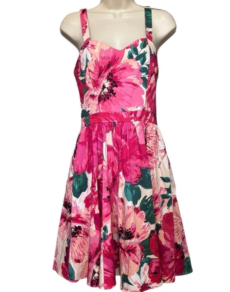 May include: A floral dress with a sweetheart neckline and a full skirt. The dress features a vibrant pattern of large pink flowers with green leaves on a white background. The dress has a fitted bodice and a flared skirt.