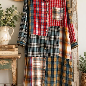 May include: A long-sleeved button-down shirt dress featuring a patchwork design of various plaid patterns in red, dark green, blue, and yellow. The garment has a collar, a single chest pocket, and light-colored buttons running down the front center.