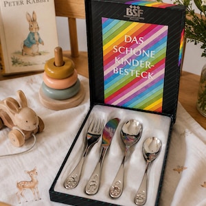 May include: A silver children's cutlery set in a black box with a rainbow design. The set includes a fork, knife, and two spoons, each with a decorative animal design. The box reads "DAS SCHONE KINDERBESTECK".
