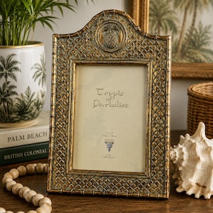 May include: An arched picture frame with a gold and dark gray lattice pattern and a pineapple emblem at the top. The frame holds a display card with the text Tropic of Paradise and 5 x 7 inches, 13cm x 18cm, with the brand name Dezine printed below.
