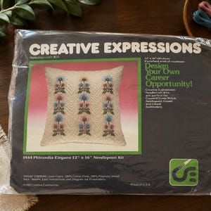 May include: A Creative Expressions needlecraft kit in a plastic package featuring a 12 inch by 16 inch cushion design with floral patterns. The dark blue packaging displays the text 1844 Phloxodia Elegans 12 inch by 16 inch Needlepoint Kit.